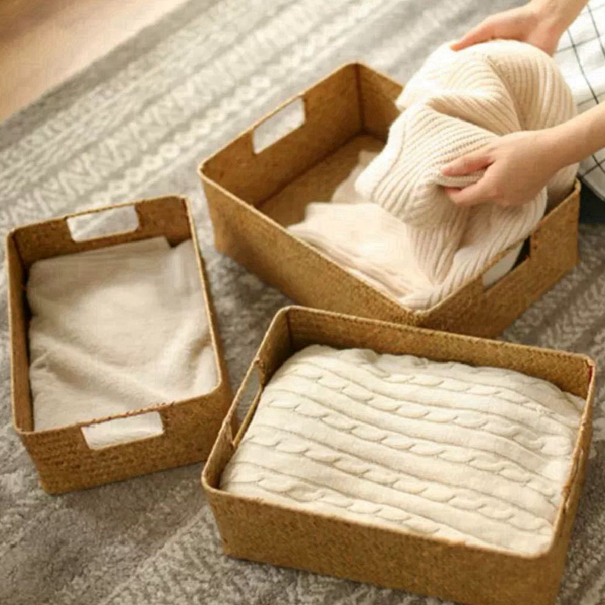 Three woven storage baskets with clothes on a textured surface