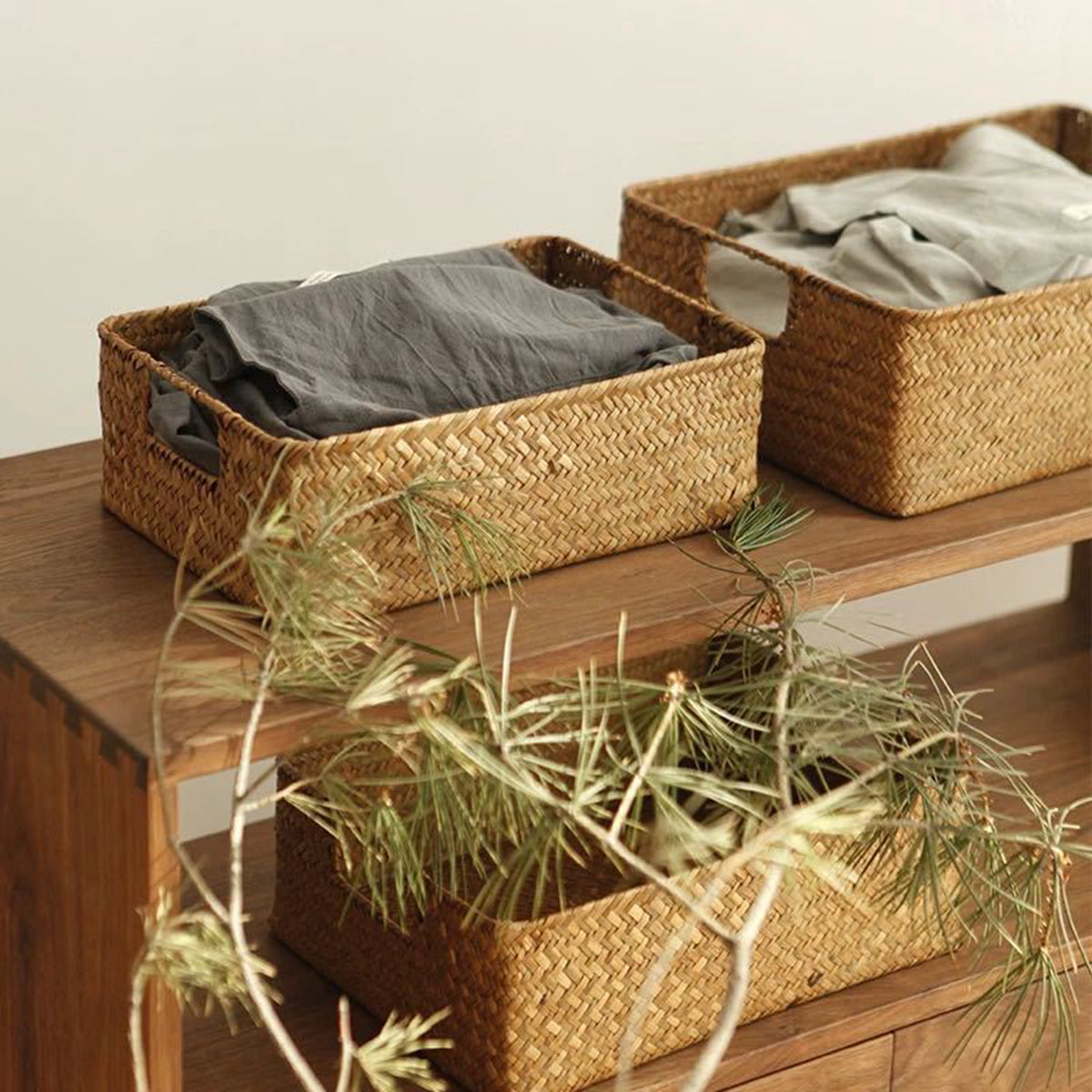 Woven baskets with folded clothes on a wooden surface, with greenery in the foreground.